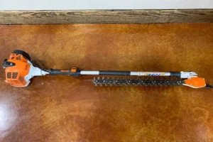 Orange extendable hedge trimmer on a wooden surface, designed for reaching tall hedges