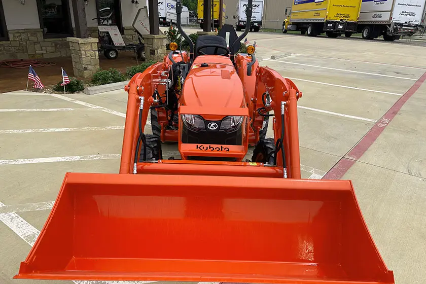 Orange Kubota tractor with front loader parked in a commercial driveway