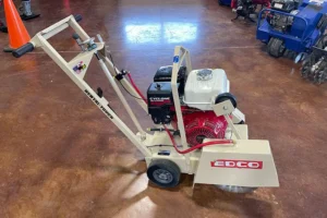 Walk-behind gas saw with a beige frame and red engine on a brown floor