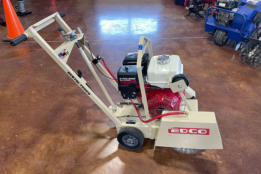 Walk-behind gas saw with a beige frame and red engine on a brown floor
