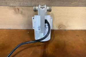 Electric waterbed pump with a black cord and metal fittings on a wooden surface