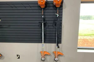 Two commercial-grade weed trimmers with orange and black design hanging on a wall